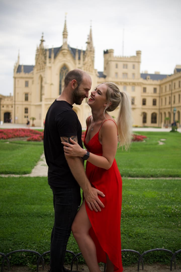 Tereza v červených šatech se směje v objetí Adama před zámkem Lednice